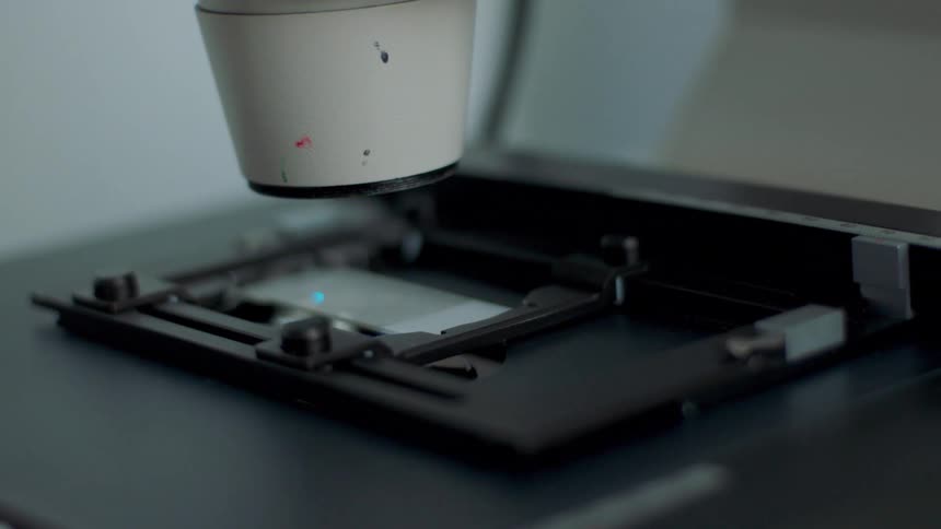 Light scans glass slides underneath a microscope