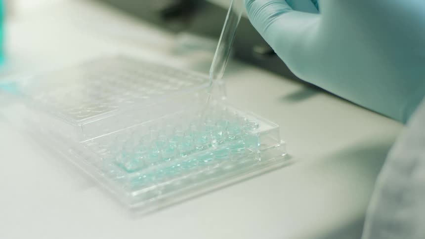 A lab worker uses a pipette to dispense blue liquid in a container