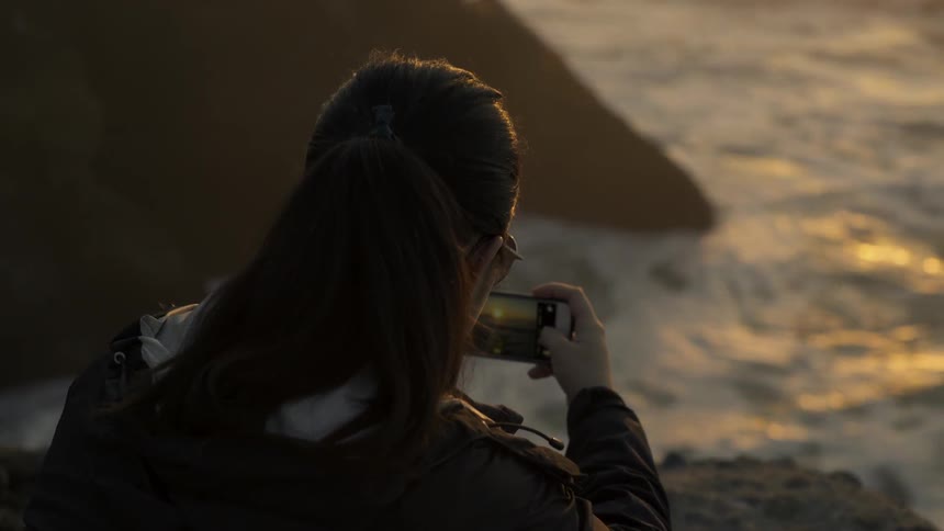 Woman taking pictures of the sea while stooping down