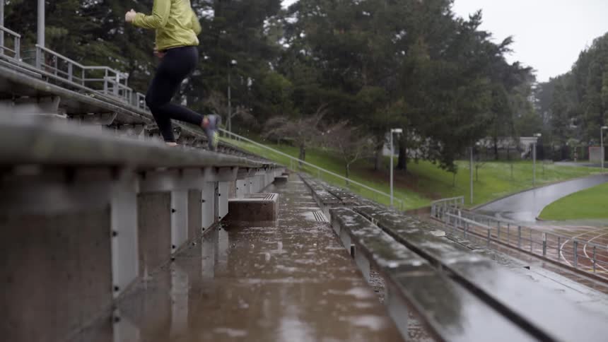 Woman jogging up wet bleacher steps in the rain with determined energy.