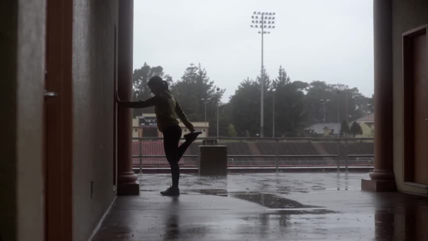 Woman stretching in the rain with focused calm and resilient energy.