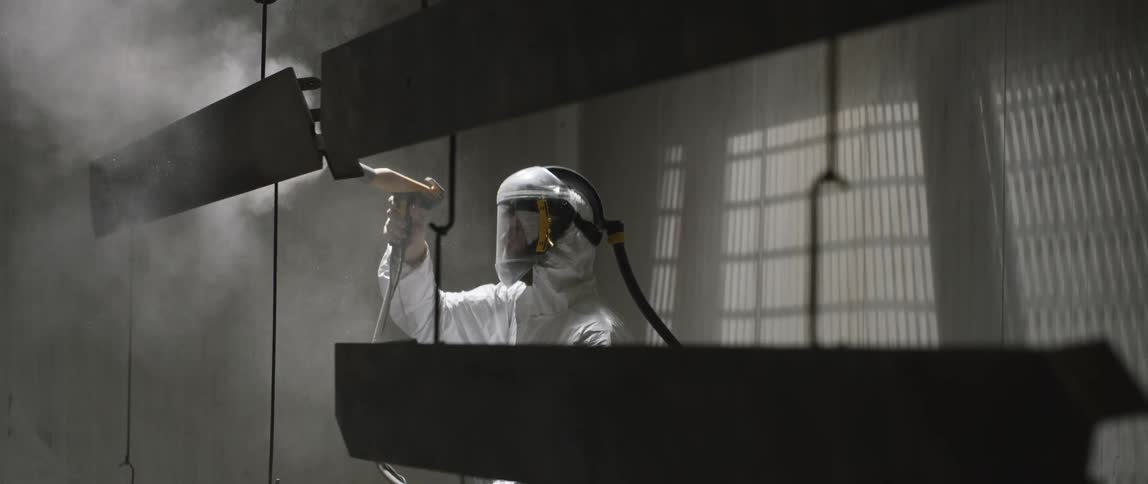 A person with a protective suit and a respirator using a hose like device that emits smoke