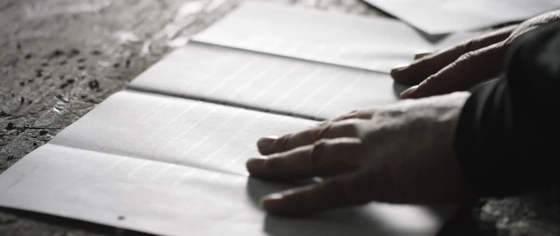 A person using their hands to smooth a sheet of paper on a table as they examine it