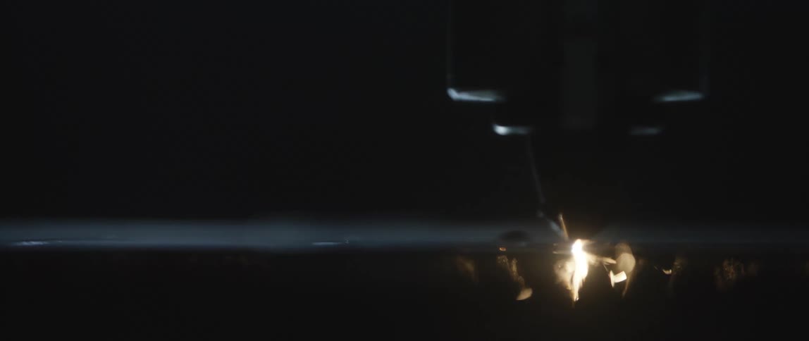 A robotic spot welder moves over a piece of metal as sparks fly