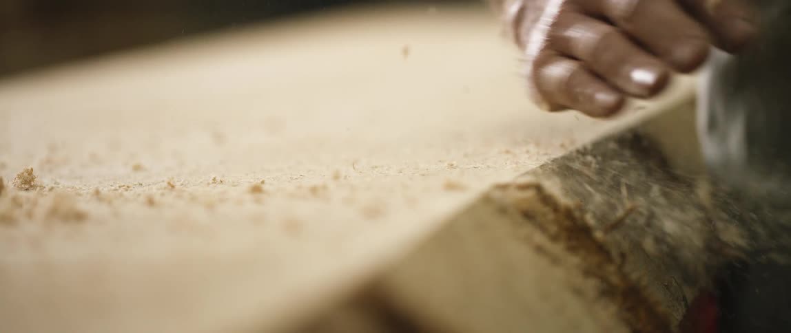 A person hand removing wood shavings from a table
