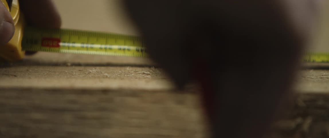 A person uses a measuring tape and pencil to mark a wooden plank