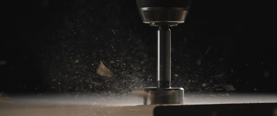 Sawdust and wood chips fly as a power drill with round bit creates a hole in a wooden plank