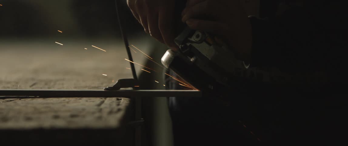 Man uses orbital sander to cut down metal bar on a workbench
