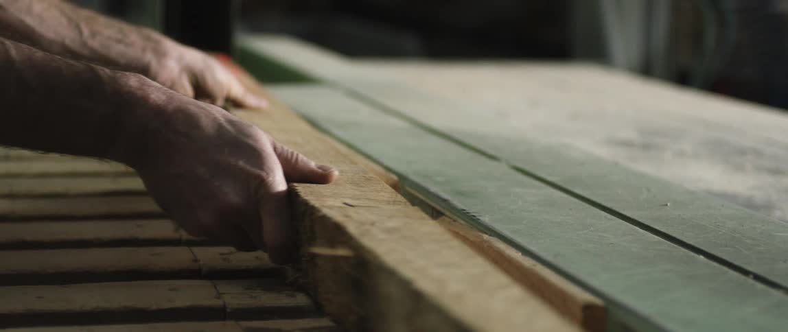 A white man slides a piece of wood into place on a saw