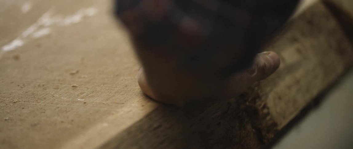 A man touches the top of a wooden plank and smooths his hand over it