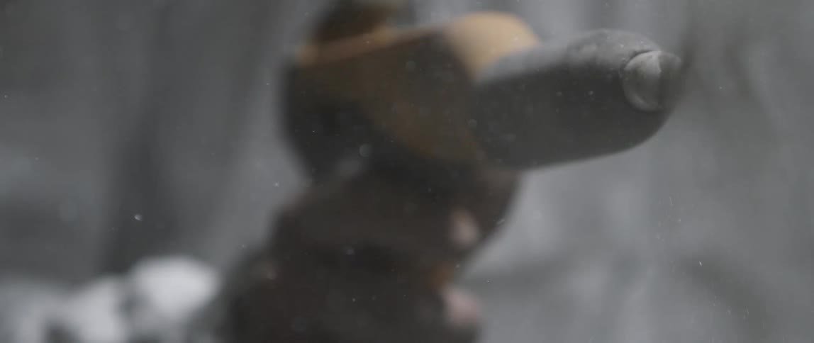 A person in protective equipment using a power tool to spray a gray substance towards the camera