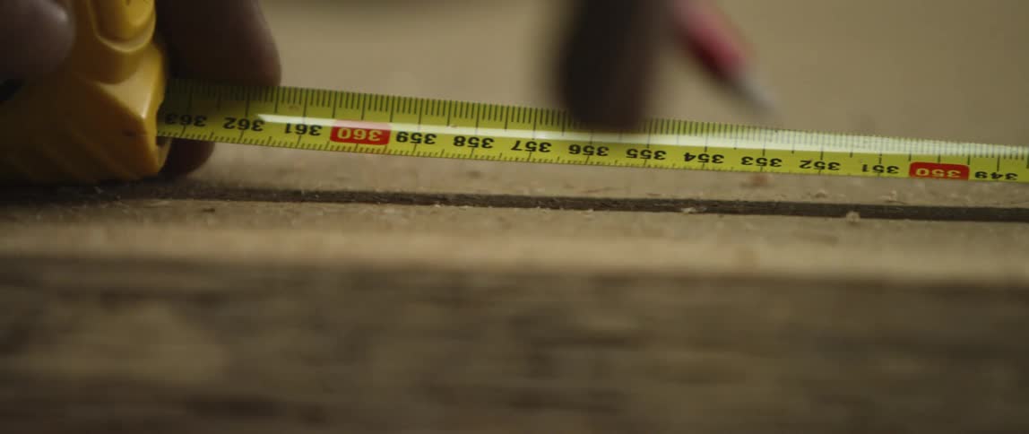Man measures the wood with a band meter and marks it with a pencil