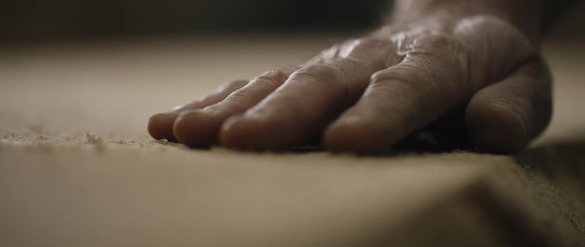 A white man rubs his hand over a piece of wood