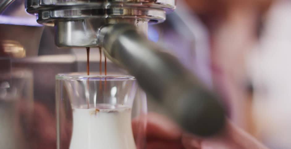 A barista places a small glass of cream under the espresso machine and it pours coffee