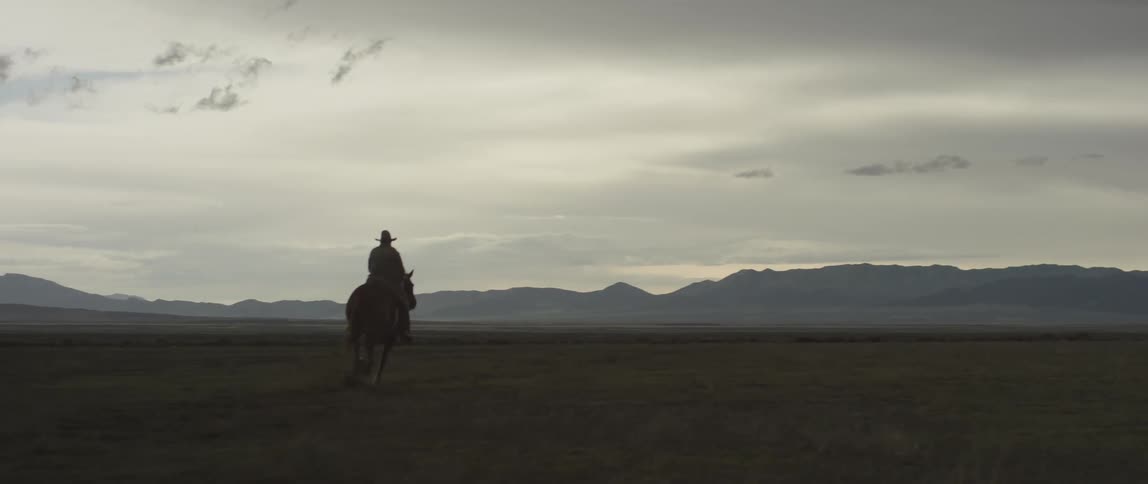 A cowboy rides a horse across a wide grassland