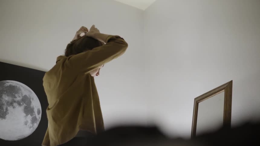 A woman is ties her hair in front of a mirror
