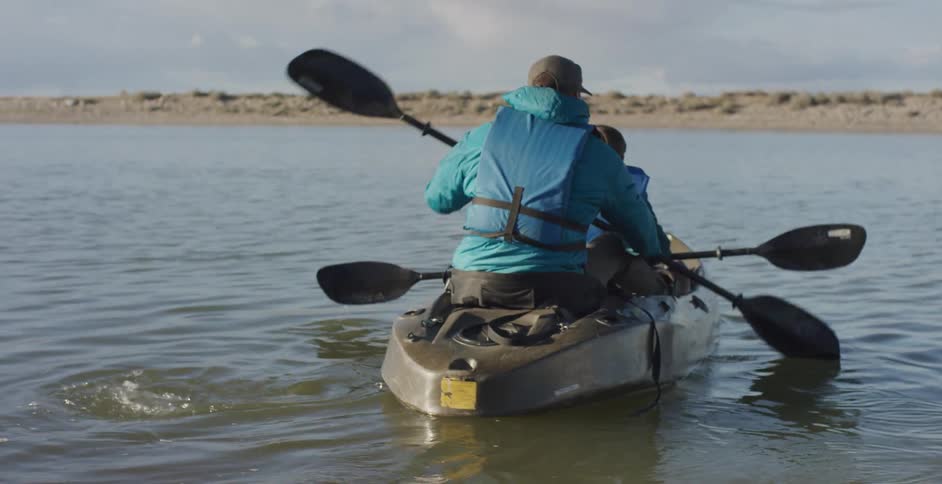 An adult and a child paddle in a canoe off the shore