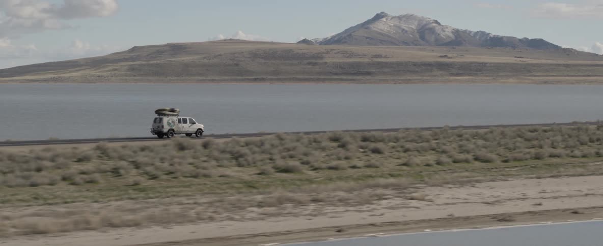 A van travels a scenic highway by a lake and mountains