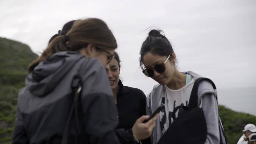 A group of women gather around a phone on a cloudy day