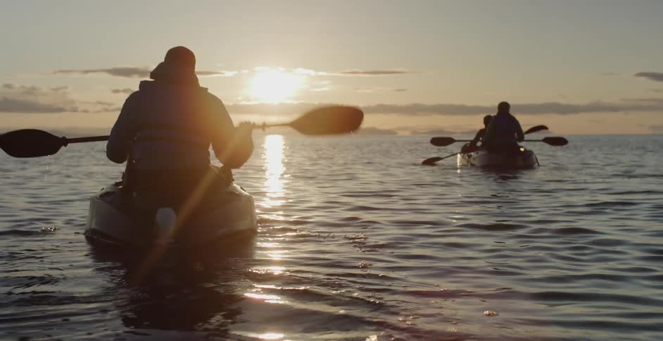 Family paddles canoes across the water at sunset