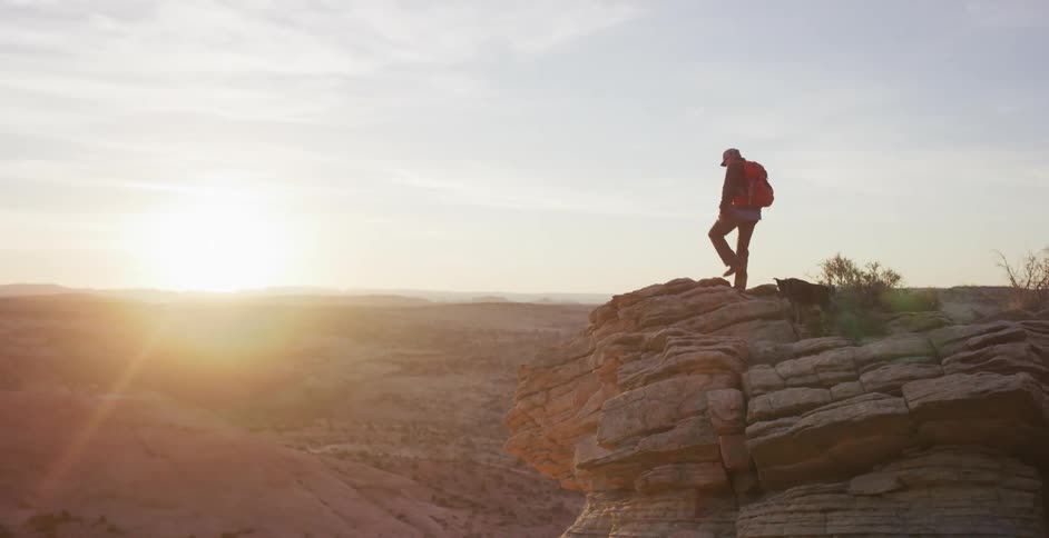A man hiking with a dog on a cliff with the sky in the background
