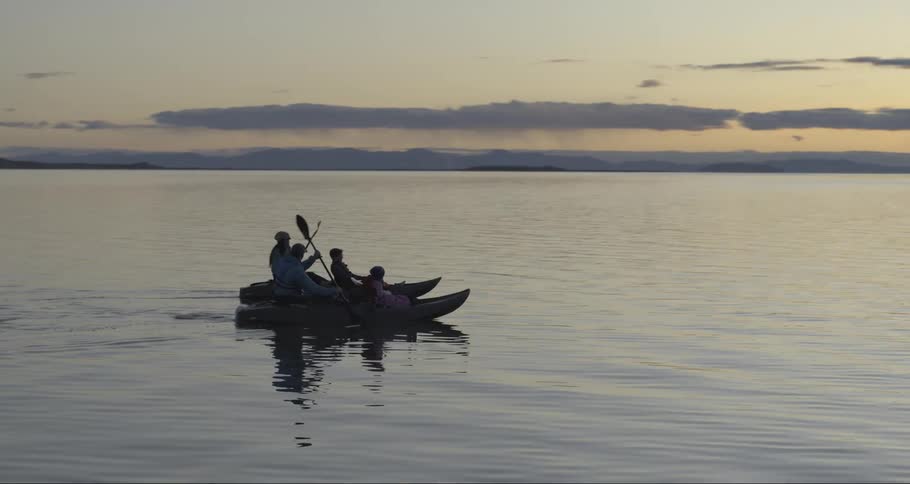 Family paddles canoes across the lake at sunset