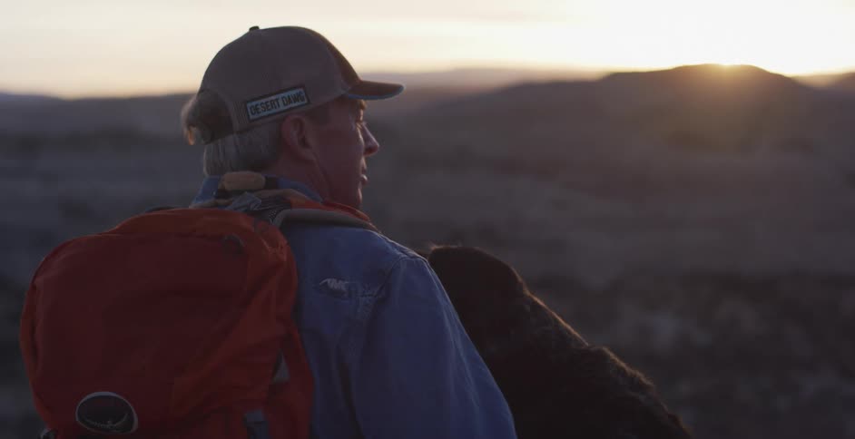 A man sits beside his dog in a mountainside terrain
