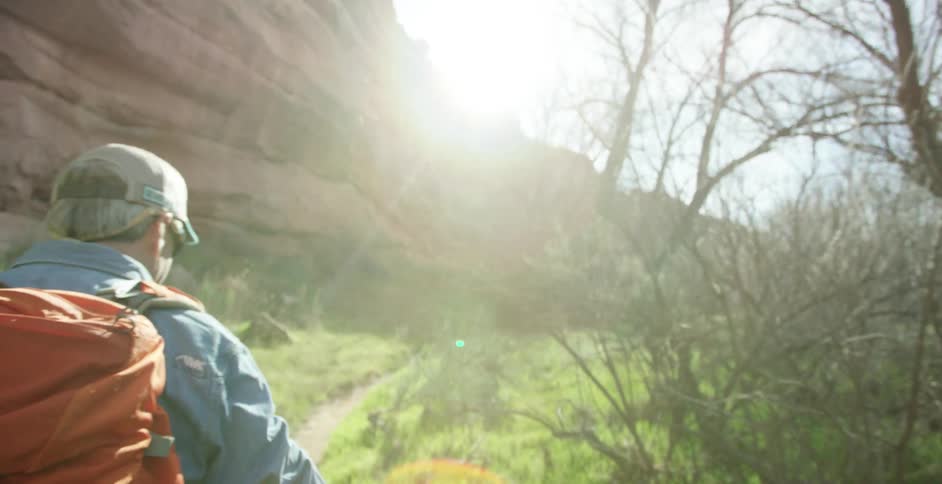 A white man hikes through a forest near a rock cliff