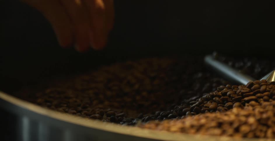 Coffee beans spin in a mixer as a white male puts his hand into the bin