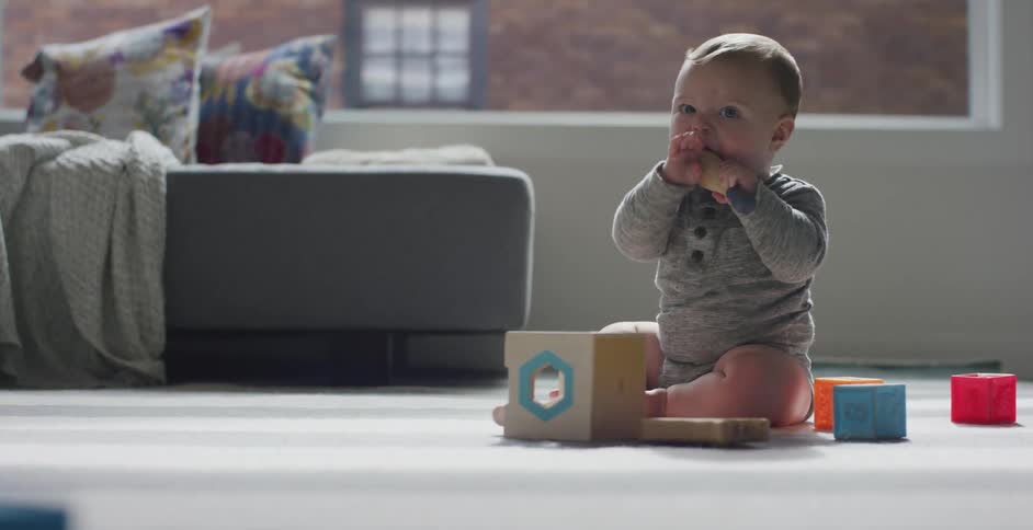 A baby sits on a floor in a home and chews on a toy