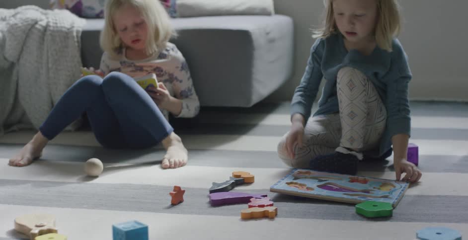 A little girl works on a puzzle while another little girl reads a book