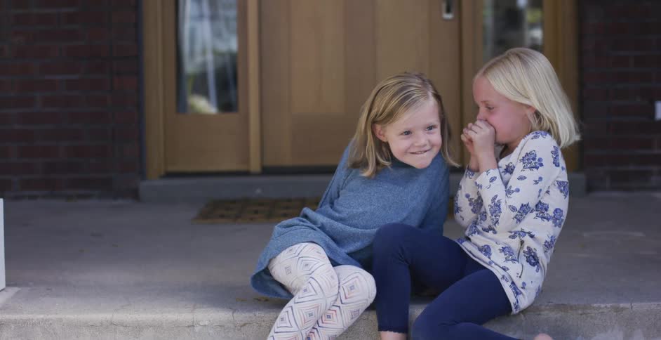 Two young girls laugh as they sit on the front steps of a house