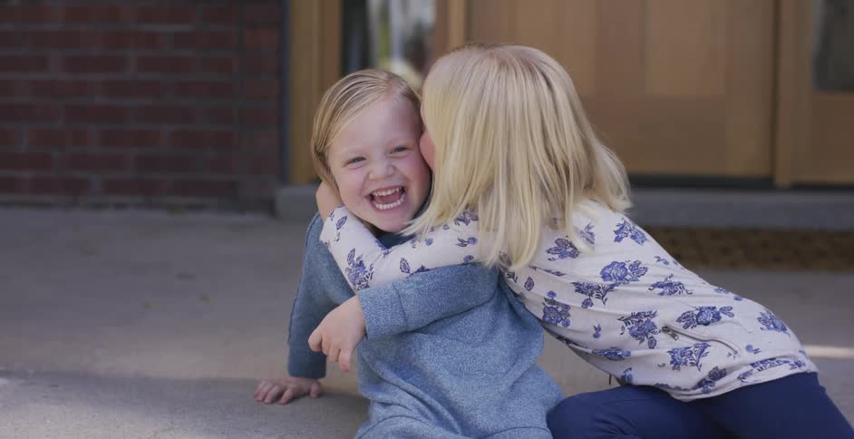 Two little girls hug and giggle while sitting on a front porch