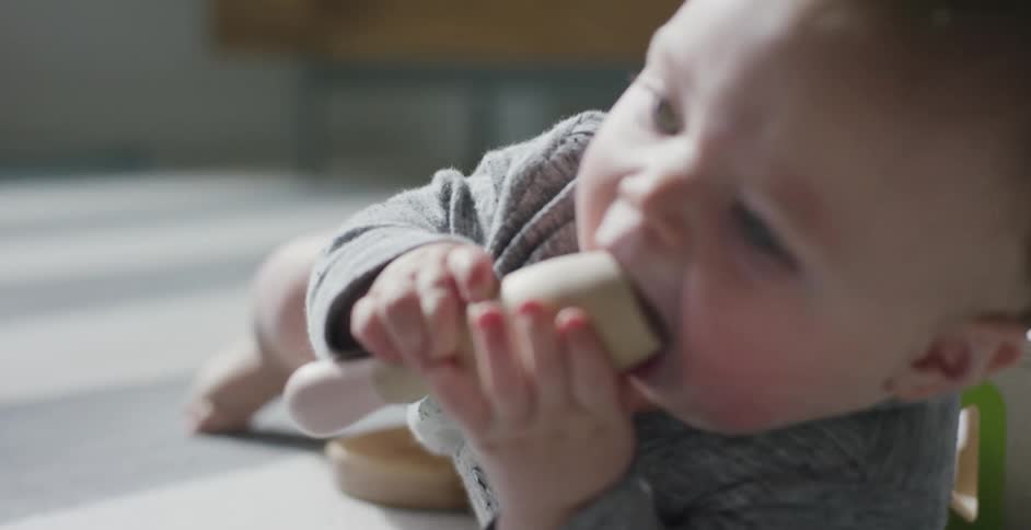 A baby lies on the floor and puts a teething toy in this mouth