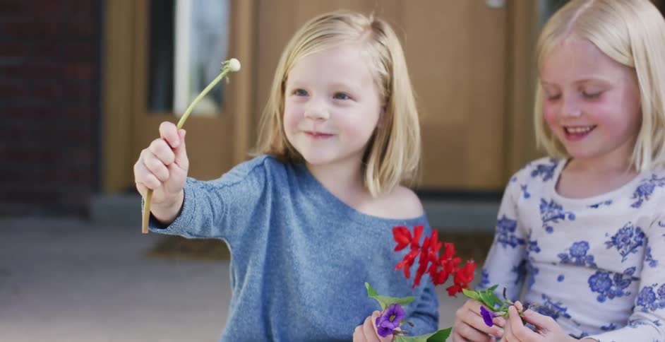 Two girls sitting in front of a house playing with flowers