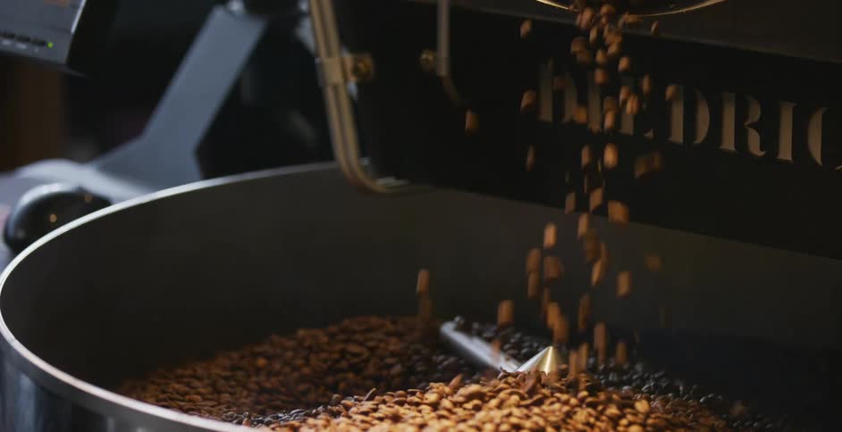 Coffee beans pouring into a metal tank with a spinning agitator