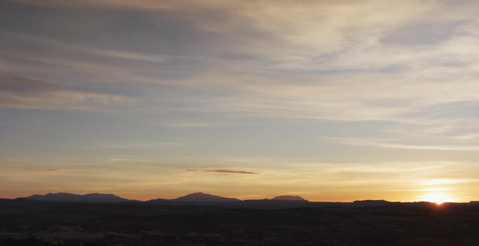 Sun begins to rise in the horizon of the desert near the mountain in the distance