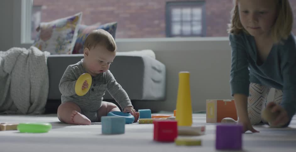 A young girl helps her baby brother play with blocks in their apartment
