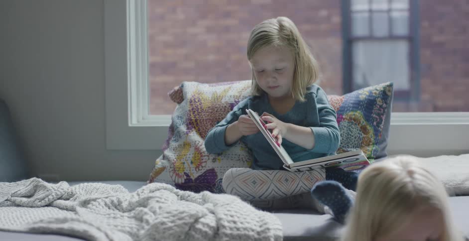 Two little girls sitting in a bedroom reading books