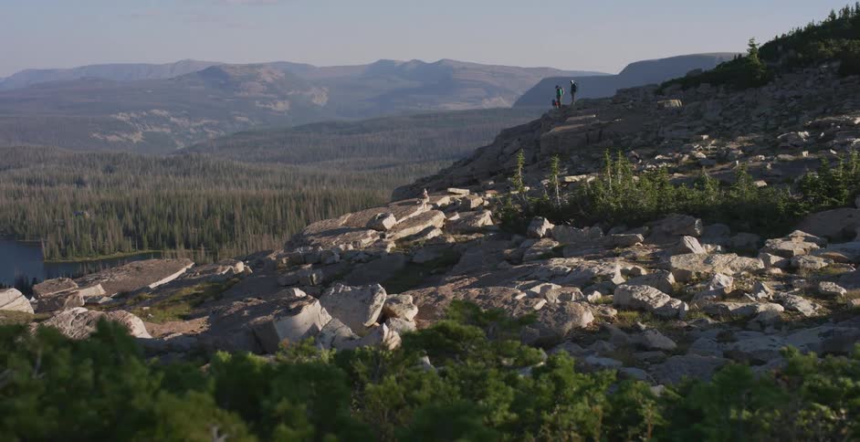 Two people stand on the slope of a mountain overlooking a valley