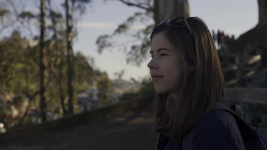 A woman is standing on a hill by some trees