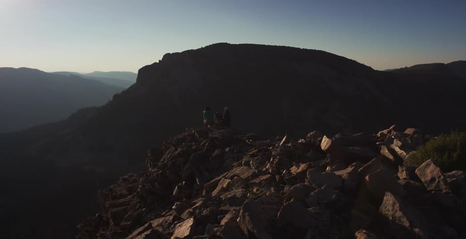 Two people climbing the rocky slopes of a mountain at sunset