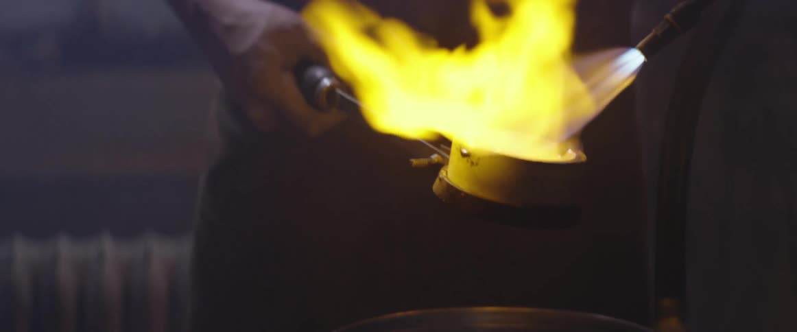 Man uses a torch to melt metal in a crucible
