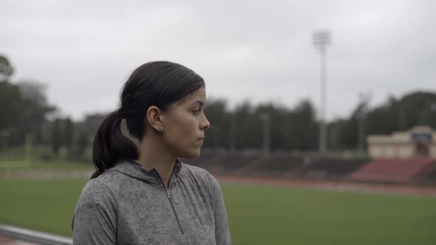 A woman stands outside in the rain on a football field