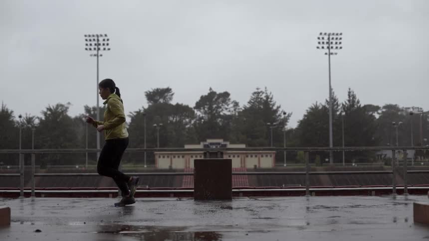 A woman runs along a platform near a stadium as it rains