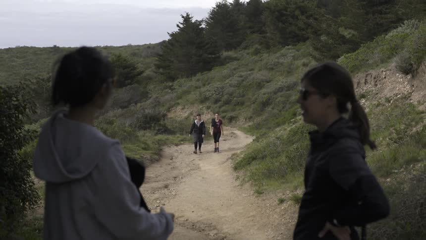 Two people hiking down a trail towards two women
