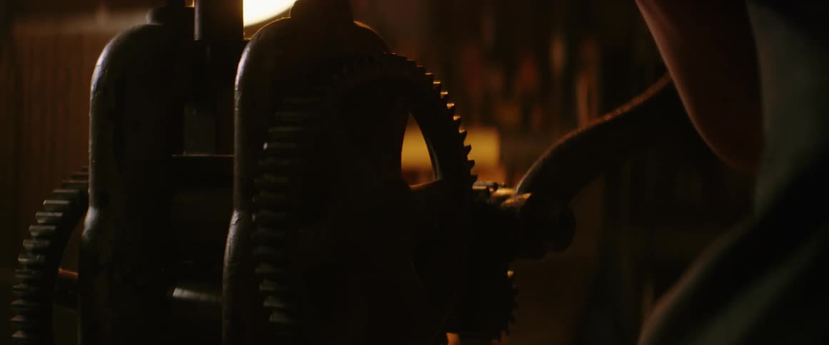 A man turns the handle of a rolling mill in his workshop
