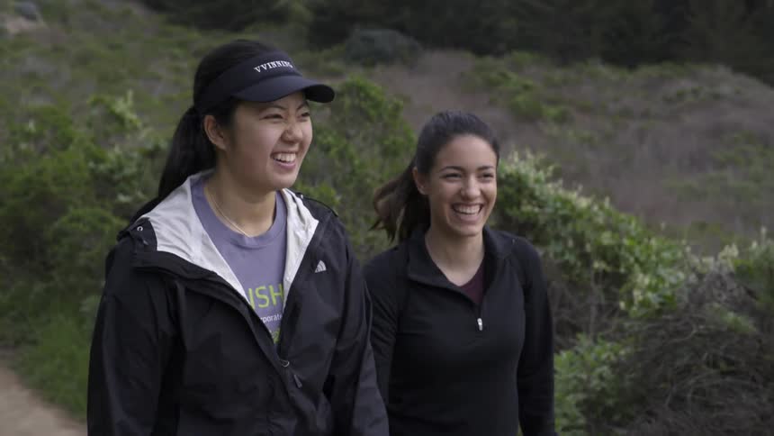 Two women holding hands walking up hill together with joyful friendship bond.