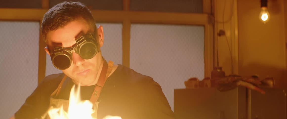 A man wearing safety goggles uses a flaming torch in his workshop