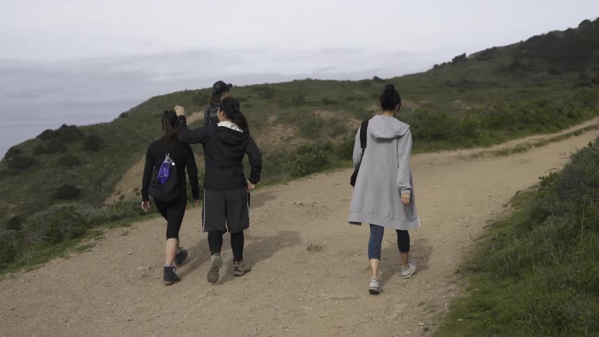 Women hiking along sandy trail together with relaxed adventurous coastal energy.